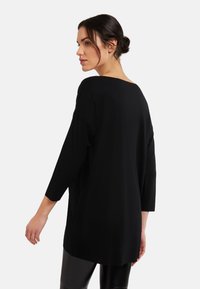 Svart oversized topp med rundad hals, trekvartsärmar och en avslappnad passform, tillverkad av mjukt, slätt material.