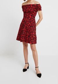 Röd axelbandslös klänning med svart leopardtryck, figursydd bodice, utsvängd kjol och korta puffärmar. Bärs med svarta spetsiga klackskor.