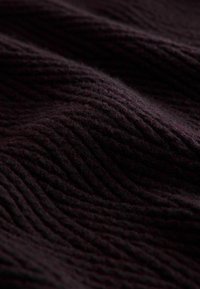 Donker bordeaux gebreide stof met gestructureerde ribbels, die een zachte, gezellige uitstraling heeft. De rijke kleur versterkt de diepte en het subtiele patroon.