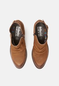 Pár hnědých kožených kotníkových bot se bočními zipy a vzorovanou podšívkou, zobrazených z vrchu na bílém pozadí.