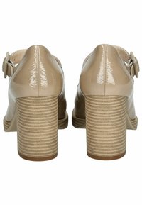 Tacchi a blocco in pelle verniciata beige con retro arrotondato, caratterizzati da fianchi inclinati e un tacco a strisce che ricorda il legno naturale. Cinturino alla caviglia regolabile.