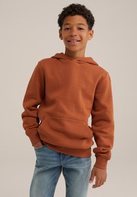 Felpa con cappuccio marrone realizzata in tessuto misto cotone, caratterizzata da una tasca a marsupio frontale e polsini a coste, abbinata a jeans blu chiaro.