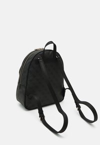 Mochila negra compacta con correas ajustables y un patrón sutil en relieve, de pie sobre un fondo blanco liso.