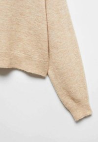 Beige Strickpullover mit weicher Textur, Rundsaum und langen Ärmeln. Der Stoff wirkt leicht und leicht strukturiert.
