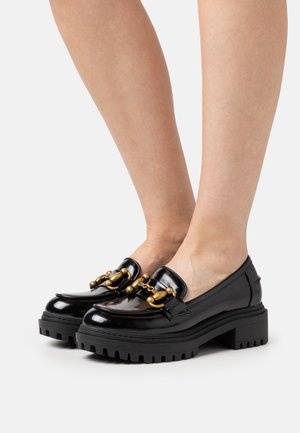Mocassins en cuir verni noir avec une semelle épaisse, dotés d'accents en métal doré à l'avant. Finition lisse avec un motif de semelle robuste.