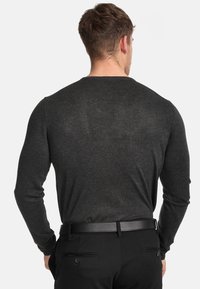 Chemise à manches longues gris foncé au design ajusté. Texture douce et couleur unie, assortie à un pantalon noir avec une ceinture et des poches.