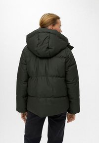 Parka acolchada de color verde oscuro con una gran capucha, textura acolchada y bolsillos laterales, que presenta un corte relajado y una tela suave.