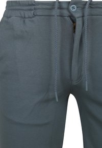 Grijze joggingbroek van zacht materiaal, met een elastische tailleband, koord, ritssluiting en een enkele voorkantzak.