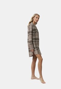 Abito camicia a quadri marroni con maniche lunghe, chiusura con bottoni, righe bianche a contrasto e orlo che arriva a metà coscia, realizzato in tessuto morbido.