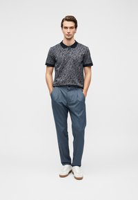 Polo à manches courtes bleu marine foncé avec un motif cachemire complexe, associé à un pantalon à fines rayures bleu clair et des baskets blanches.