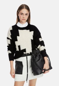 Schwarzer und cremefarbener gestrickter Pullover mit abstraktem Muster, kombiniert mit einem weißen strukturierten Minirock mit schwarzen Akzenten und einer schwarzen Bucket Bag.