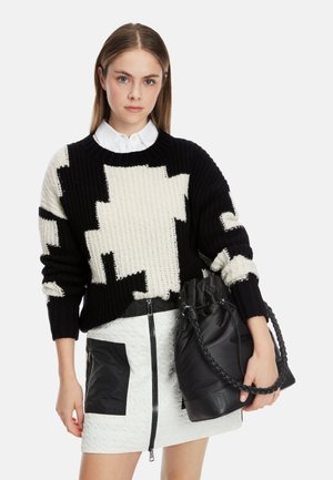 Black and cream knitted sweater with abstract pattern, paired with a white textured mini skirt featuring black accents and a black bucket bag.