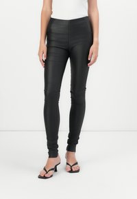 Leggings neri in finta pelle con vestibilità slim, vita alta e polsini alla caviglia, abbinati a sandali neri con cinturini. Texture liscia, senza pattern visibili.