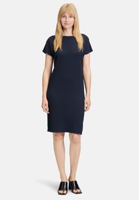 Robe en tricot bleu marine à manches courtes, coupe droite, motif texturé, longueur genoux, associée à des chaussures noires ouvertes à bout libre.