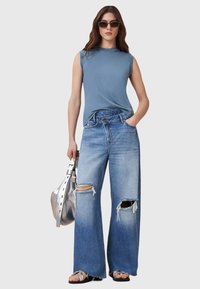Top senza maniche di colore azzurro chiaro abbinato a jeans in denim larghi e distressed. Gli accessori includono una borsa argentata e occhiali da sole scuri.