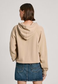 Sudadera con capucha beige de diseño corto y mangas largas, combinada con una falda de mezclilla que cuenta con bolsillos traseros y un lavado azul.