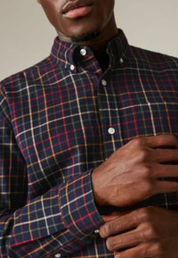 Camicia di cotone a quadri in blu navy, rosso e giallo. Presenta colletto con bottoni, tasca anteriore e maniche lunghe con polsini. Tessuto con motivo testurizzato.