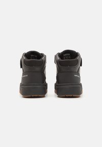 Černé středně vysoké tenisky s texturovaným svrškem, suchým zipem a gumovou podrážkou se hnědým akcentem. Branding na patě a boku.