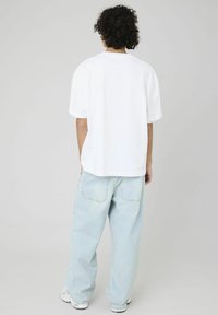 T-shirt blanc à manches courtes avec une coupe décontractée, associé à un jean baggy bleu clair. Le t-shirt a un ourlet droit et une texture douce et lisse.