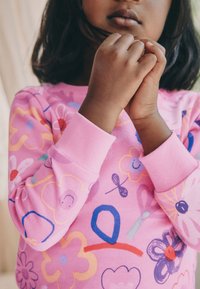 Roosa pikkade varrukatega särk, millel on värvikas lillemuster, mis sisaldab erinevaid kujundeid, mustreid ja aktsente lillakas, punases ja sinises toonis.