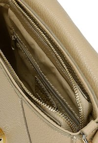 Wnętrze beżowej skórzanej torebki z wieloma zamykanymi na suwak przegrodami. Posiada złote akcesoria, pikowane wykończenie oraz gładkie tekstury.