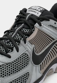 Os tênis Nike Vomero 5 apresentam um cabedal em malha cinza, acabamentos texturizados, atacadores pretos e um logo swoosh preto de lado.