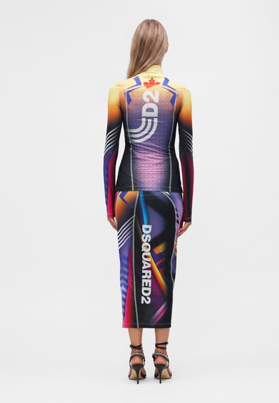 Femme en haut coloré ajusté à manches longues et jupe assortie avec logos DSQUARED2, debout dos au spectateur, portant des sandales noires à talons hauts.