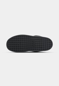 Black sneaker sole with textured grid pattern and central rectangular logo embossed on a plain white background.