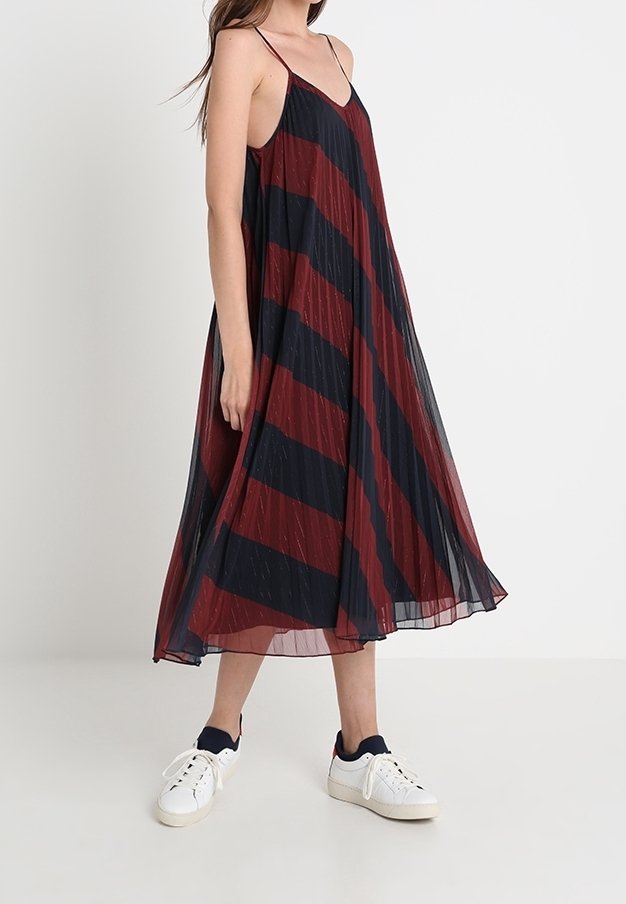 Randig maxikjol i mörkröd och marinblå, med tunna remmar, en flödande silhuett och ett lätt, strukturerat tyg. Bärs med vita sneakers.
