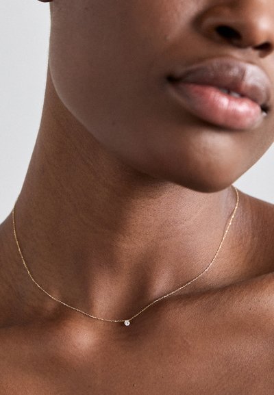Guldkæde med en lille diamantpendant, delikat design, glat tekstur og minimalistisk æstetik.