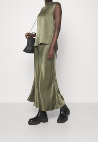 Top senza maniche in satin verde oliva abbinato a una gonna midi coordinata. Finishing testurizzato, vestibilità ampia e stivali chunky neri. Inclusa una borsa nera.