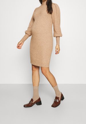 Femme portant une robe-pull beige côtelée avec manches bouffantes, des chaussettes beiges et des mocassins à talons carrés en cuir verni marron.
