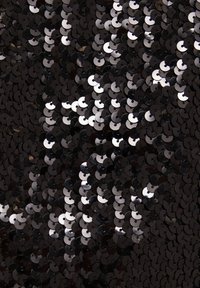 Gros plan sur des sequins noirs et argentés densément accolés, créant une surface brillante et réfléchissante avec des formes circulaires qui se chevauchent.