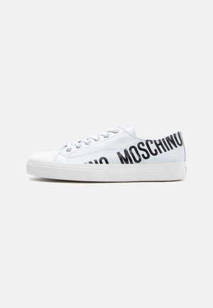 Biały niskoprofilowy sneaker z czarnym napisem "MOSCHINO" po boku i białymi sznurowadłami, na jednolitym jasnoszarym tle.