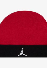 Rød strikket hue med en sort foldet kant, med en hvid broderet Jumpman-logo. Glat tekstur og ribbet design over det hele.