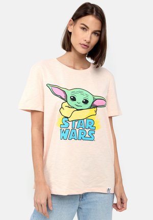 Lyserød t-shirt med en tegnefilmsfigur med store grønne ører og sorte øjne, centrert tekst "STAR WARS" i blå, korte ærmer, afslappet pasform.