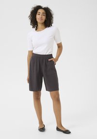 Top bianco a maniche corte abbinato a pantaloni corti grigio scuro al ginocchio con una vita elasticizzata e due tasche frontali. Texture del tessuto liscia.