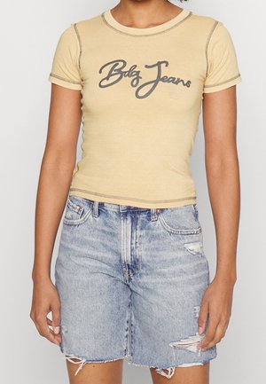 Geel aansluitend T-shirt met grijze "Bdg Jeans" tekst, korte mouwen en contrasterende stiksels, gecombineerd met lichtblauwe, versleten denim shorts.