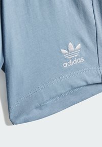 Svetlomodré bavlnené tričko s krátkymi rukávmi, s bielou vyšitou logom Adidas a rovnom lemom, textúrovaná látka a viditeľné švy.