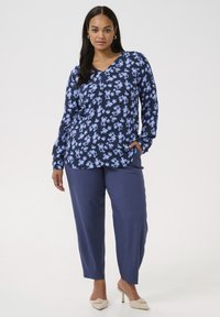 Blusa floral en color marino con flores azules, escote en V y mangas largas. Combinada con pantalones de pierna ancha en color marino y zapatos de tacón beige.