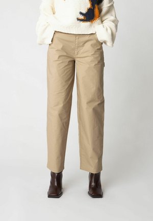 Beige tapered trousers with a textured finish, featuring a relaxed fit and side pockets, paired with high-heeled ankle boots.