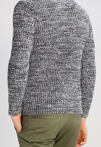 Maglione lavorato a maglia in bianco e nero, con un motivo testurizzato. Maniche lunghe e orlo a coste. Abbinato a pantaloni verde oliva.