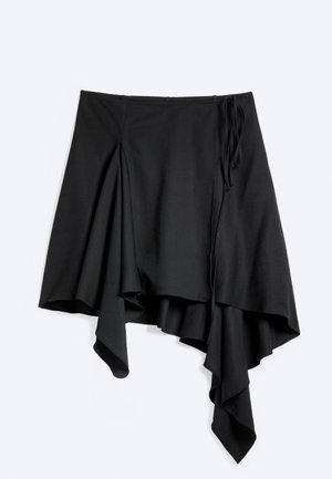 Jupe noire asymétrique avec tissu drapé et détail de nœud sur le côté, présentant un ourlet irrégulier avec des couches fluides.