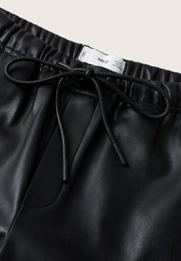 Joggers en simili cuir noir avec une taille élastique et un cordon de serrage. Texture lisse avec un léger brillant et sans motifs visibles. Étiquette positionnée à l'intérieur.