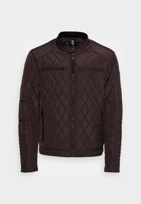 Giacca trapuntata marrone scuro con colletto alto, dotata di due tasche sul petto con zip e dettagli a coste sulle spalle. Design aderente con polsini a costine.