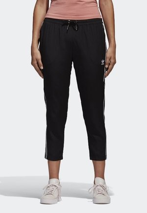 Černé zkrácené sportovní kalhoty s elastickým pasem, stahovací šňůrkou a bílými bočními pruhy. Vytvořené s lehkými sportovními teniskami.