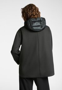 Czarny płaszcz z teksturowanym, pikowanym kapturem. Charakteryzuje się minimalistycznym designem, gładkim materiałem i uporządkowaną sylwetką.