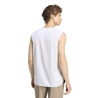 Jeune homme portant une chemise blanche texturée sans manches et un pantalon beige, de dos et regardant vers la droite sur fond blanc.