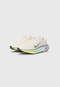 Chaussures de course Nike avec une tige en mesh crème, un logo swoosh marron, et une semelle multicolore en dégradé. Présentent des contours arrondis et une surface texturée.