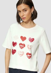 Witte katoenen t-shirt met een voorkantafbeelding van negen harten in verschillende tinten rood en roze, met textuur van lipafdrukontwerpen.
